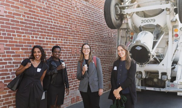 Four Carbon Forward Summit attendees smiling beside a brick wall and a concrete mixer truck