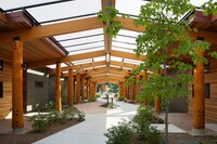 a view down the wide, open corridor of the longhouse with apartments on either side, filled with greenery. large logs support a gabled roof.