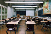 Empty classroom with rows of desks, chalkboards covering the walls, a pull-down world map and no visible windows.