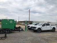 Two white pick-up trucks charging at an EV charging station.
