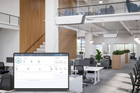 Picture of an office with two white, rectangular air filter units hanging from wires. Lines drawn around the units lead to a display unit superimposed onto the image, representing data connectivity.