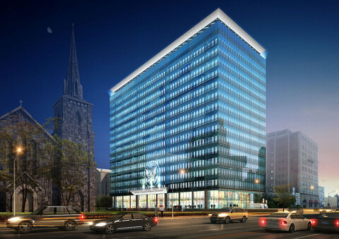  A rectangular glass building with an eagle crest above the door, lit up with blue light at night with traffic going by in front.
