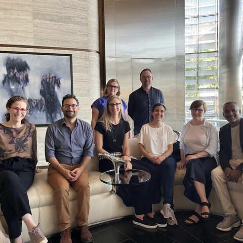 group photo shows five smiling people on a couch and two smiling people standing behind.