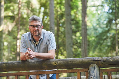 Jason McLennan leaning on a railing with trees in the background