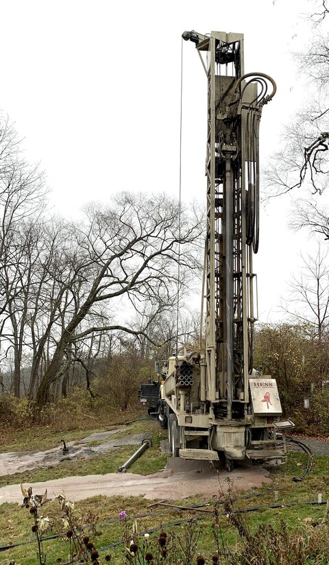 construction equipment shown from the back a tall, thin attachment in the foreground will soon be used to drill deep wells for ground-source heat pump installation.