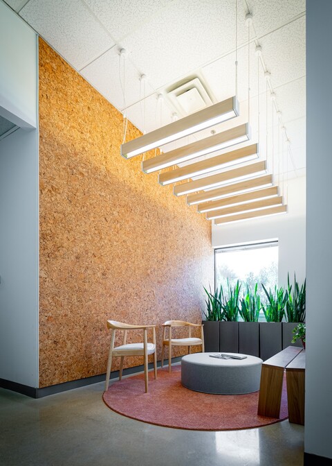 A rectangular room with a series of long, slim, wood luminaires hanging from cables in a row from tall ceilings.