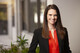 white woman in red blouse and black suit jacket with long dark hair.